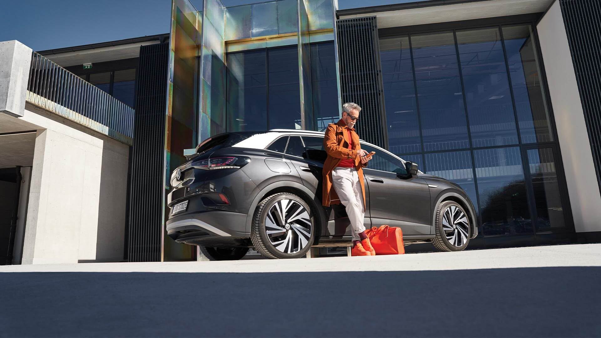 Un uomo con abito elegante e borsa da lavoro passa davanti alla sua Volkswagen Passat GTE per uso aziendale